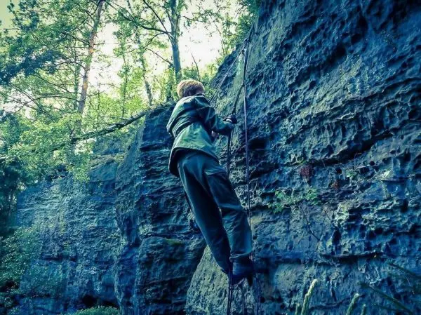 Klettert an einer Felswand mit einer selbstgebauten Seilbrücke