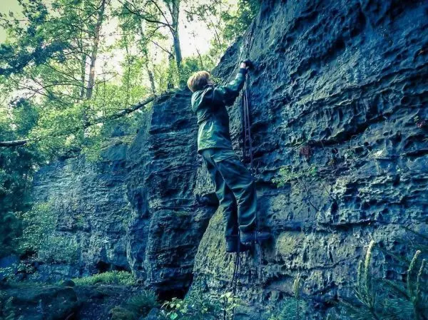 Klettert an einer Felswand mit Hilfe von Seilen und Ästen