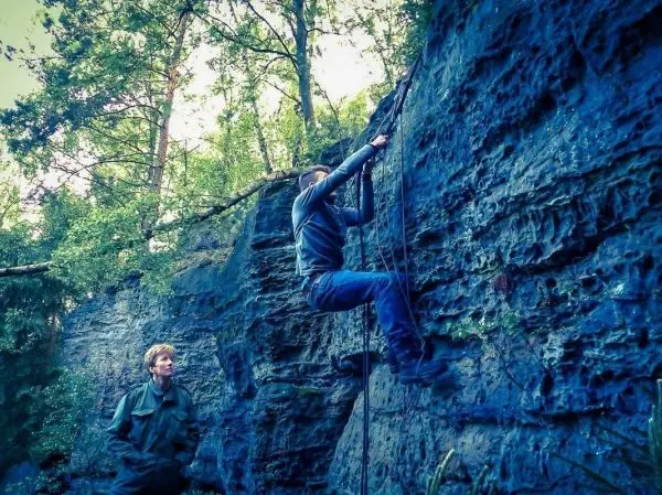 Klettert an einer Felswand mit Seilunterstützung, beobachtet von einer Person