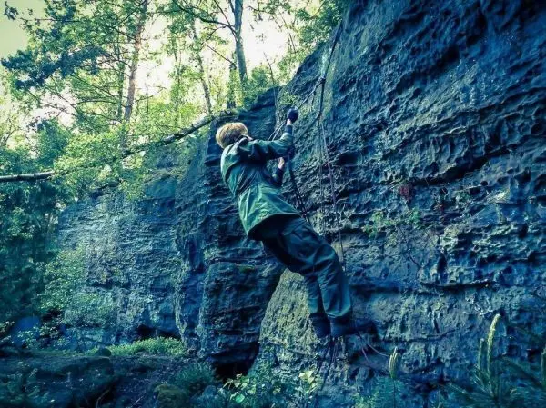 Klettert an einer Felswand mit Seilunterstützung in bewaldeter Umgebung