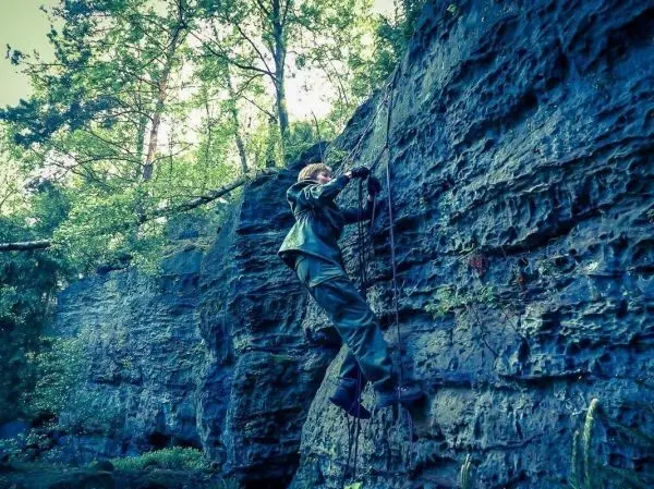 Klettert an einer Felswand mit Seilunterstützung und Handschuhen