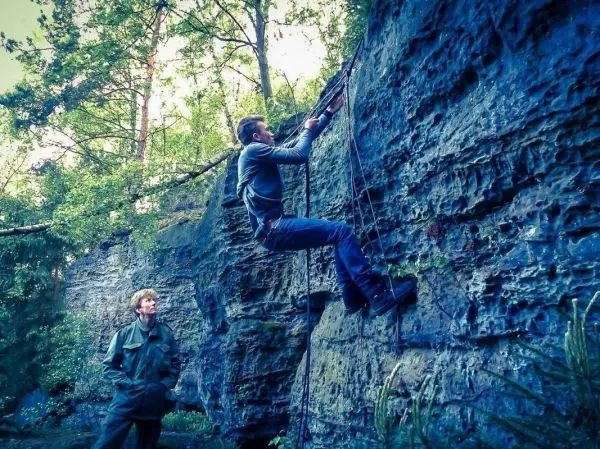 Klettert an einer Felswand mit Seilunterstützung, während ein Beobachter zusieht