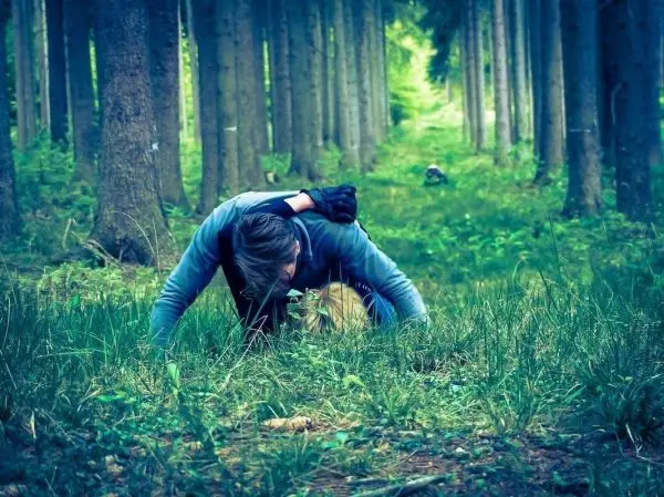 Kriechende Person im Gras zwischen Bäumen in einem Waldgebiet