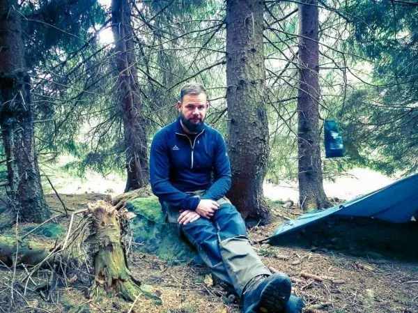 Mann sitzt auf einem Stein neben einem Tarp im Wald