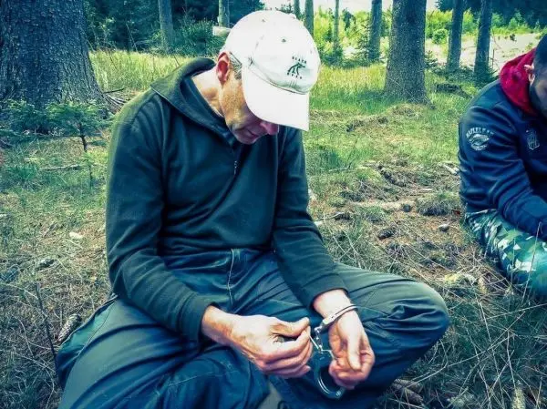 Mann sitzt im Wald und versucht, Handschellen zu öffnen