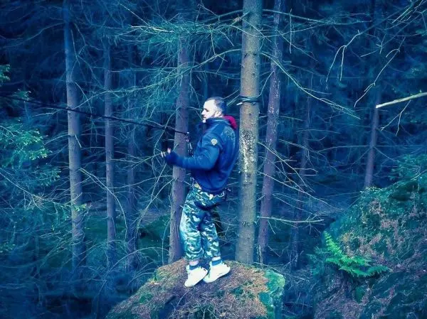 Mann steht auf einem Felsen und hält ein Seil zwischen zwei Bäumen