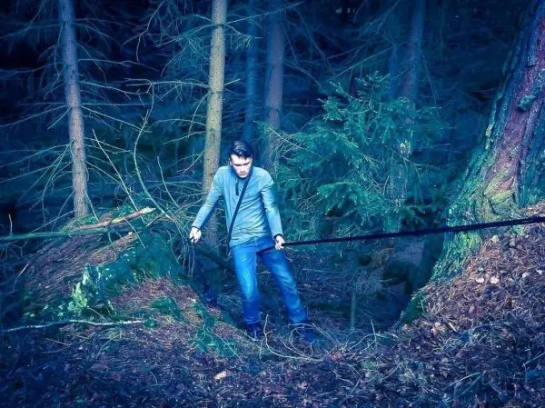 Mann zieht an einem Seil über einen Erdgraben im Wald