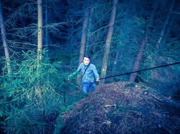 Mann zieht sich an einem Seil einen Hang im Wald hinauf