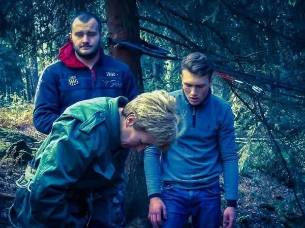 Person beugt sich vor, während zwei Personen zuschauen im Wald