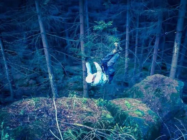 Person hängt kopfüber an einem Baum im Wald