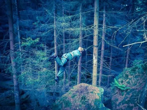 Person hängt zwischen Bäumen über einem Felsen