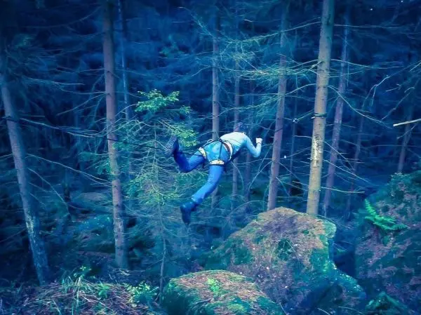 Person in Klettergurt überquert an einem Seil zwischen Bäumen über Felsen