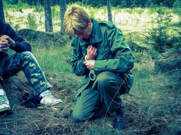 Person kniet im Gras und hält ein Werkzeug in der Hand