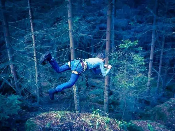 Person schwingt an einem Seil zwischen Bäumen