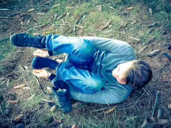 Person sitzt auf dem Boden und bindet einen Schuh im Wald