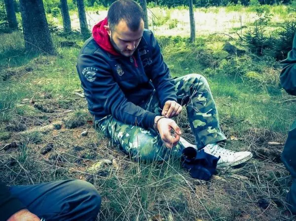 Person sitzt im Gras und knotet eine Schnur beim Überlebenstraining