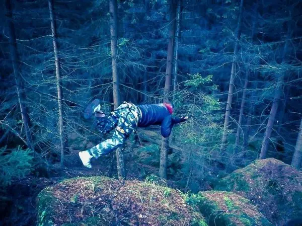 Person springt von einem Felsen zwischen Bäume im Wald