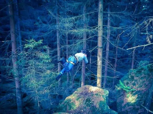 Person überquert eine selbstgebaute Seilbrücke zwischen Bäumen