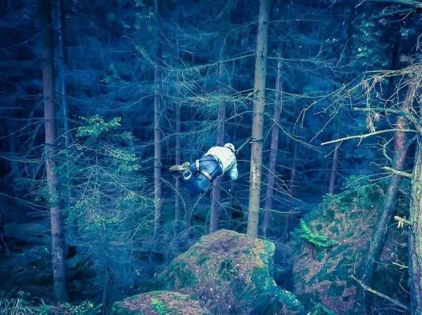 Person überquert eine selbstgebaute Seilbrücke zwischen Bäumen