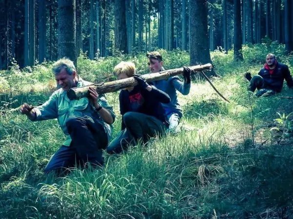 Personen tragen einen langen Stock durch den Wald beim Survival Training