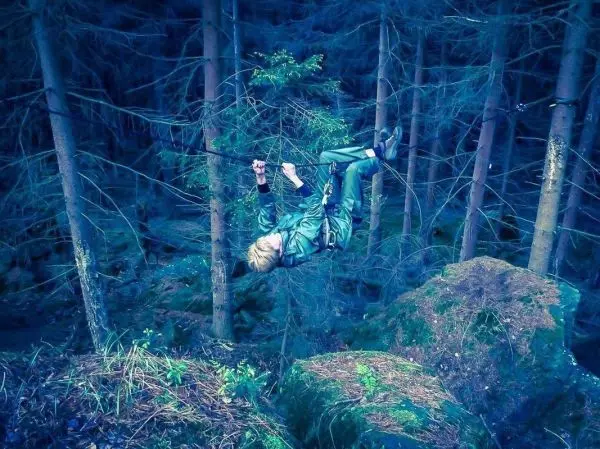 Selbstgebaute Seilquerung über Felsen im Wald, Person hängt daran