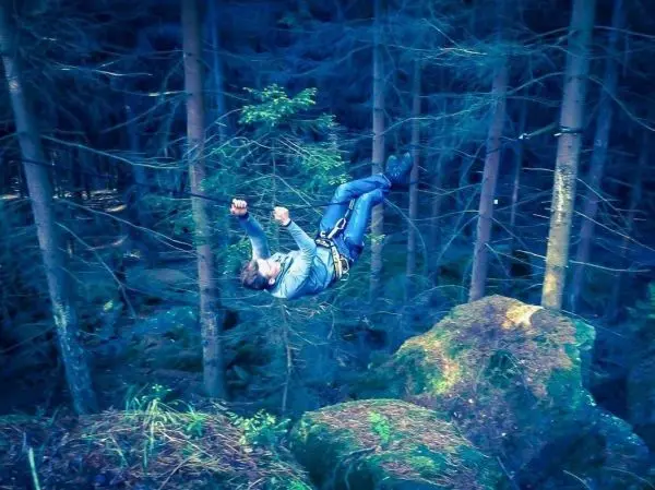 Selbstgebaute Seilquerung über Felsen im Wald, Person hängt gesichert in der Luft