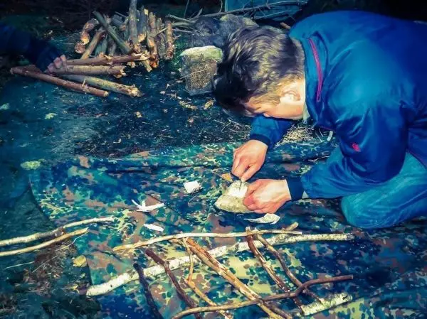Stein wird mit einem Messer bearbeitet, während Holzstücke auf einer Plane liegen