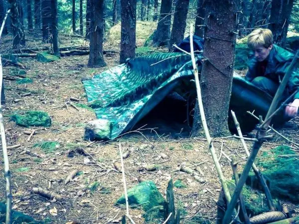 Tarp-Notunterkunft wird zwischen Bäumen aufgestellt, während jemand daran arbeitet