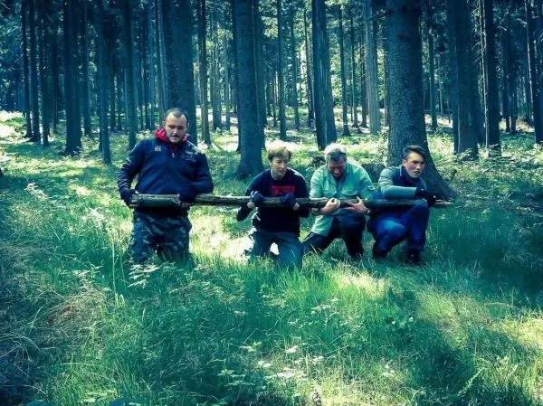 Vier Personen halten Holzstücke in einer Waldlandschaft, kniend im Gras