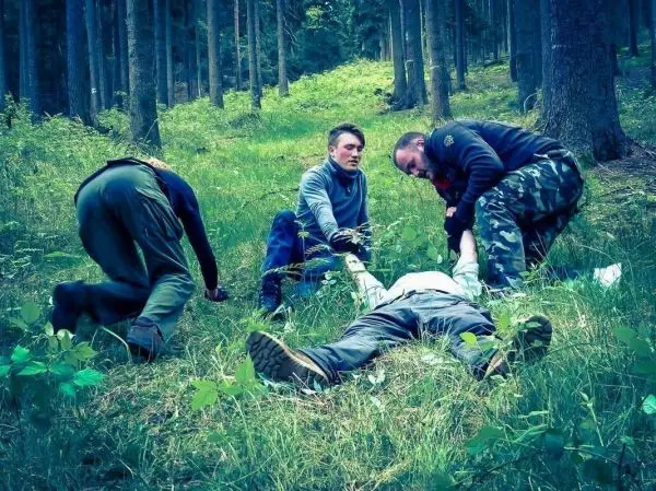 Vier Personen leisten Erste Hilfe an einer liegenden Person im Wald