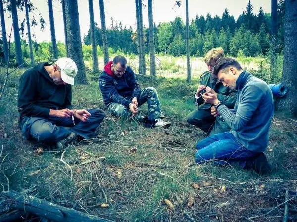 Vier Personen sitzen im Wald und bearbeiten Zunder mit Messern