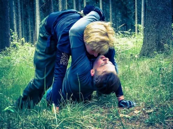 Zwei Personen im Bodenkampf auf grasbewachsenem Boden zwischen Bäumen