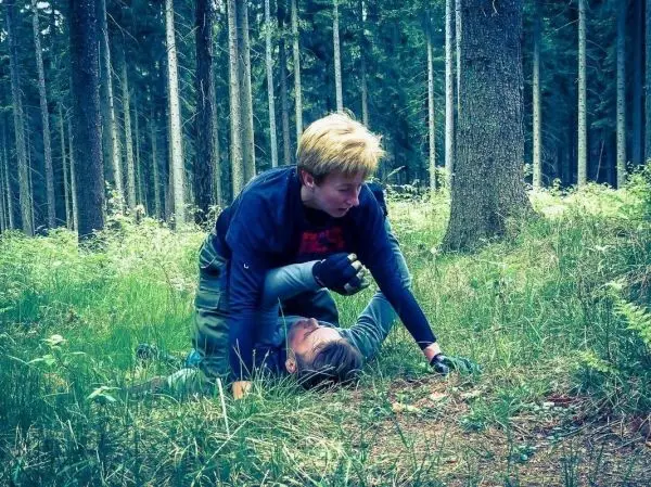 Zwei Personen im Wald, eine Person kontrolliert die andere am Boden