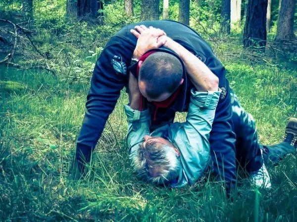 Zwei Personen im Wald üben eine Bodenkampftechnik auf weichem Untergrund