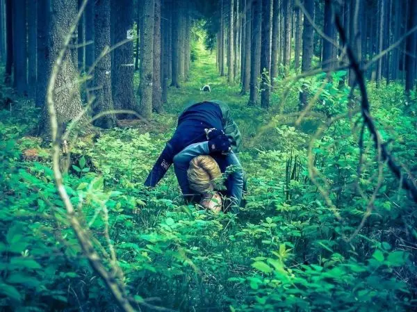 Zwei Personen in einem Wald, eine kniet auf dem Boden und die andere beugt sich über sie
