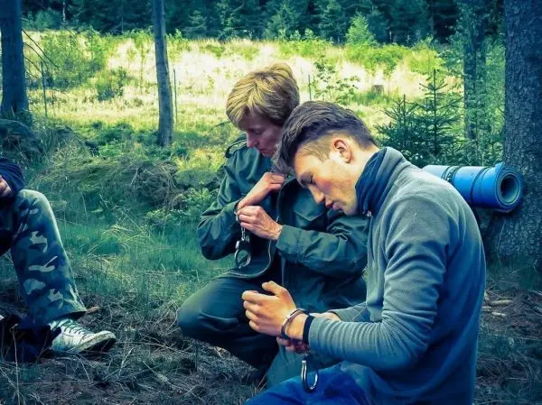 Zwei Personen knien im Wald und beschäftigen sich mit Handschellen