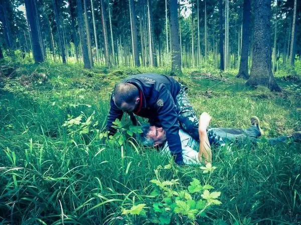 Zwei Personen liegen im Gras, eine Person hält die andere am Boden fest