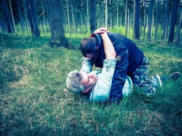 Zwei Personen liegen im Gras und führen eine Bodenkampftechnik aus