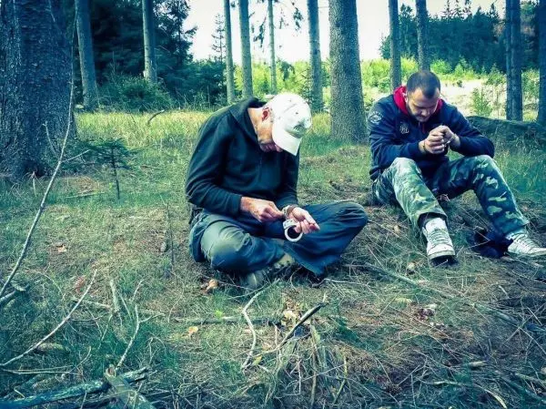 Zwei Personen sitzen im Wald und bearbeiten Holzstücke mit Messern
