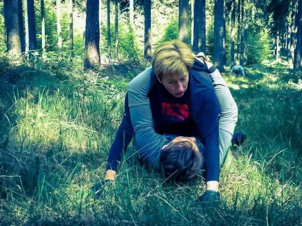 Zwei Personen üben eine Bodentechnik im Wald auf Grasboden aus