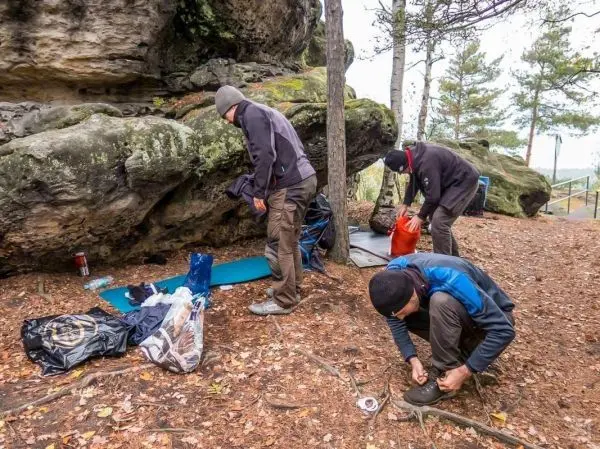 Drei Personen bereiten Ausrüstung unter einem Felsen im Wald vor