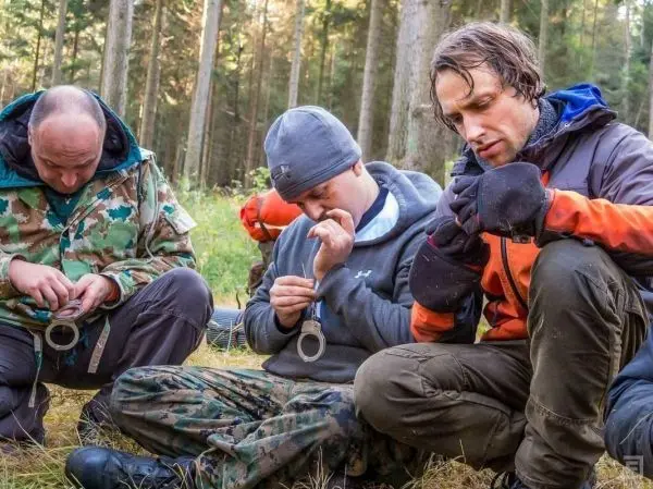 Drei Personen konzentrieren sich auf das Fädeln von Handschellen in einem Wald