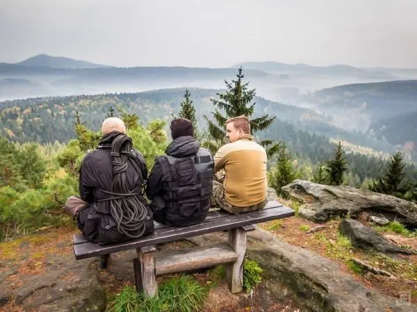 Drei Personen sitzen auf einer Bank und blicken auf eine bewaldete Landschaft