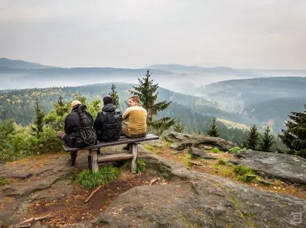 Drei Personen sitzen auf einer Bank und blicken auf eine bewaldete Landschaft
