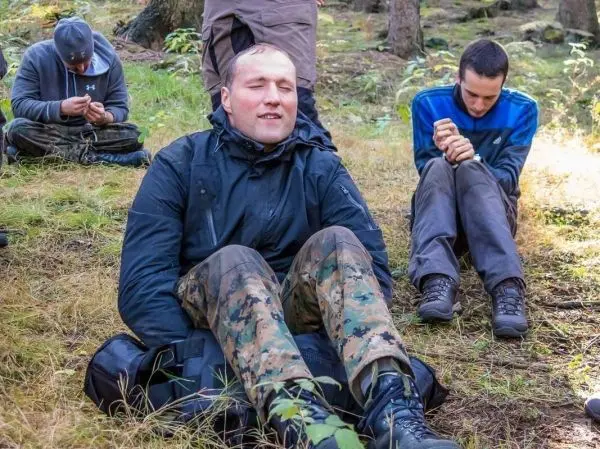 Drei Personen sitzen im Wald auf dem Boden und beschäftigen sich mit Ausrüstung