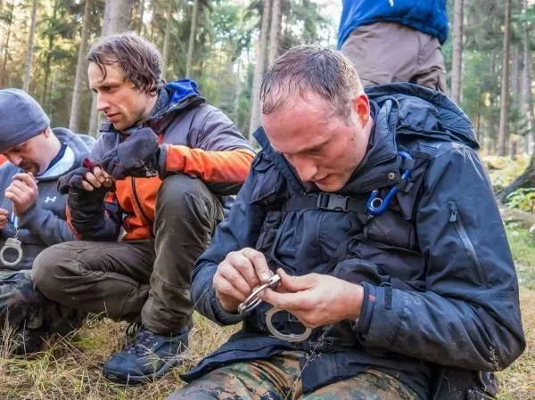 Drei Personen sitzen im Wald und beschäftigen sich mit Handschellen