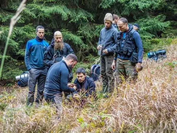 Gruppe betrachtet Bodenpflanzen im Wald, Rucksäcke liegen im Hintergrund