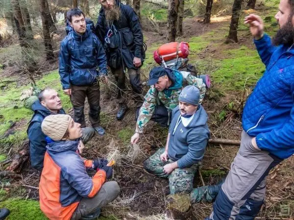 Gruppe diskutiert um ein Zundernest im Wald, einige halten Werkzeuge in der Hand