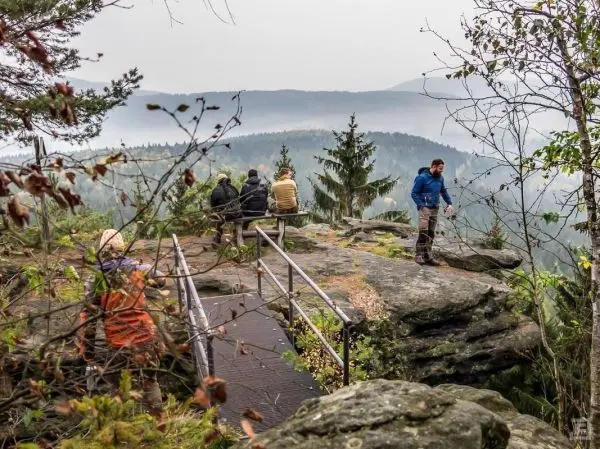 Gruppe sitzt auf Felsen mit Aussicht, eine Person steht daneben und schaut hinaus