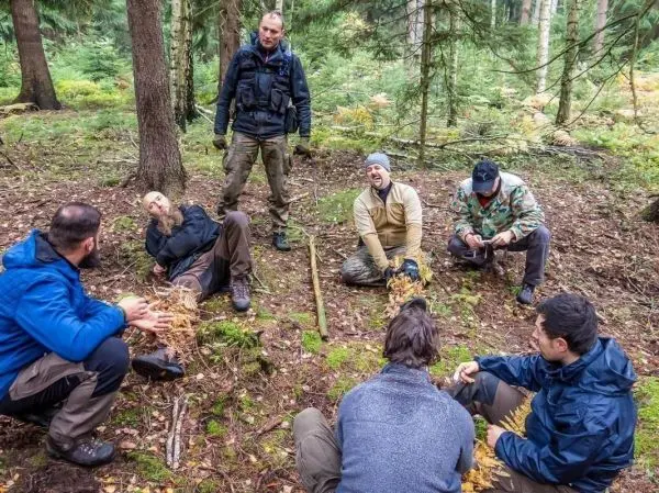 Gruppe sitzt im Wald auf dem Boden und diskutiert, einige halten Pflanzen in der Hand
